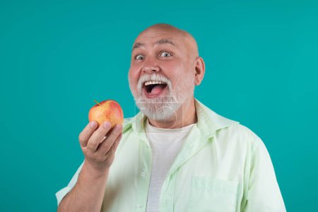 Téléchargez les photos : Grand-père aîné drôle manger des pommes en studio. Portrait d'un homme âgé mangeant une pomme. Un homme qui mord des pommes. Pommes pour personnes âgées. Senior sur l'alimentation et un mode de vie sain. Portrait sénior aux pommes - en image libre de droit