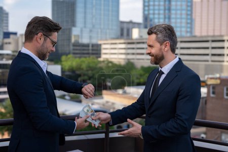 Photo for Businessman giving money to his partner outdoor. Businessman giving money. Teamwork. Business partnership. Rich business man in suit with money dollar bills. Giving money concept. Illegal corruption - Royalty Free Image