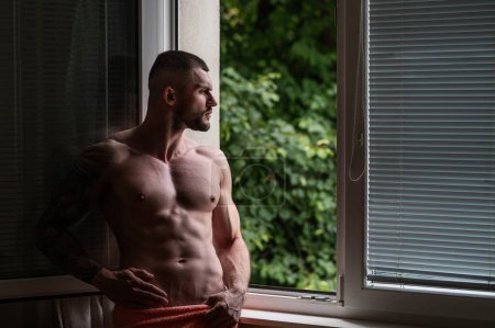 Foto de Sexy and naked muscular young man posing on window curtains. Sexy shirtless male model. Attractive young naked man body. Romantic dreaming nude male model with sexy body - Imagen libre de derechos