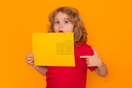 Photo for Child showing blank banner on yellow isolated background . Advertising billboard, placard. Child hold empty color blank sheet of paper, copy spase. Poster for your text information. Amazed emotions of - Royalty Free Image