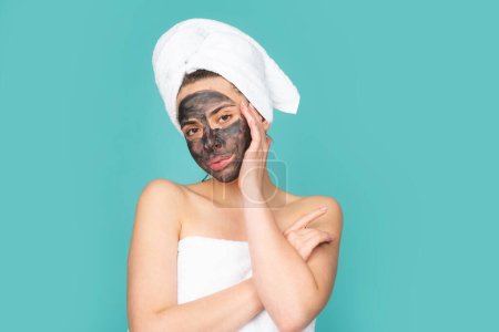 Téléchargez les photos : Femme appliquer masque facial charbon de bois masque isolé sur fond bleu studio. Spa, masque cosmétique. Belle femme avec masque facial en argile noire. Soin de la peau, peeling, hydratation et soins de beauté - en image libre de droit