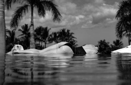 Téléchargez les photos : Femme dans la piscine à débordement. Jeune fille profitant d'un soleil au bord de la piscine. Vacances, vacances, bains de soleil, détente de voyage concept de repos. Loisirs d'été, mode de vie sain - en image libre de droit