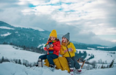 Téléchargez les photos : Les enfants apprécient l'hiver, jouer avec la randonnée en traîneau dans la forêt d'hiver. Les enfants jouent avec la neige. Concept vacances d'hiver - en image libre de droit
