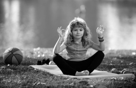Photo for Kid doing meditate yoga asana on roll mat in park. Kids girl practicing doing yoga outdoor. Child boy training yoga - Royalty Free Image