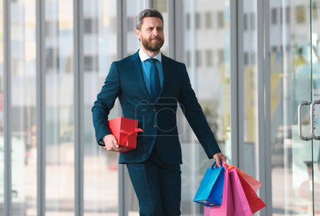 Photo for Business man shopping in a shopping center. Happy businessman in suit holding paperbags. Shopaholic man walking on commercial street with a lot of shopping bags - Royalty Free Image