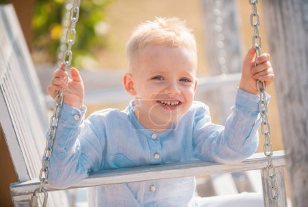 Foto de Niño divirtiéndose en un columpio. Adorable niño divirtiéndose en un columpio al aire libre. Niño rubio, cara de emoción sonriente - Imagen libre de derechos