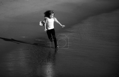 Téléchargez les photos : Happy kid running on sea beach. Funny boy run along surf edge. Active kids lifestyle. Little runner exercising. Sporty young child jogging and training outdoor - en image libre de droit