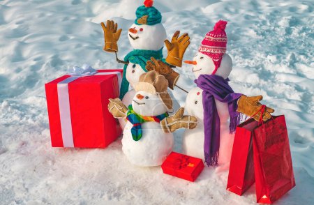 Téléchargez les photos : Joyeux Noël et bonne année carte de vœux avec copie-espace. Bonhomme de neige de famille souriant heureux - concept de réduction de vente. drôle groupe de bonhommes de neige famille tenir cadeau de Noël - en image libre de droit