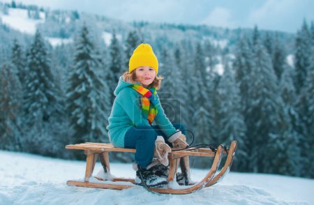 Téléchargez les photos : Joli garçon profitant d'une balade en traîneau. Luge d'enfants, équitation d'un jeu de luge à l'extérieur dans la neige sur le paysage hivernal. Amusement actif d'hiver extérieur pour des vacances en famille - en image libre de droit