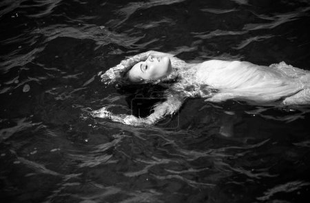 Foto de Mujer joven flotando en el océano o en el agua de mar, relajándose y cuidándose. Retrato de moda de elegante chica linda en vestido de verano durante las vacaciones en el complejo de lujo - Imagen libre de derechos
