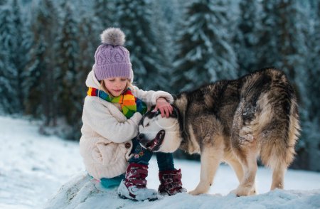 Téléchargez les photos : Fille s'amuser avec le chien en hiver. Enfants mignons jouant avec animal de compagnie en plein air. Activités hivernales pour les enfants - en image libre de droit