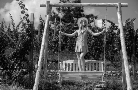 Foto de Mujer despreocupada disfrutar del verano. Chica de moda en banco de madera. Mujer relajante al aire libre en el columpio porche en la naturaleza. Humor de verano - Imagen libre de derechos