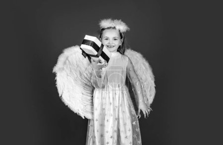 Foto de Angel niña con alas blancas Niño lindo bebé con alas de ángel. Niños ángel con regalo presente, retrato de estudio. Pequeño ángel rubio con alas blancas sostiene regalo. Tarjeta de regalo Valentine - Imagen libre de derechos