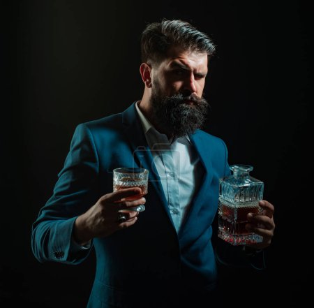Téléchargez les photos : Tablier barman en cuir tenant cocktail whisky en verre. Hipster avec barbe et moustache en costume boit de l'alcool après la journée de travail - en image libre de droit