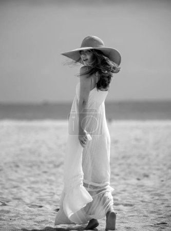 Téléchargez les photos : Modèle d'été posant sur la plage. Robe d'été vêtements femme à la mode. Jeune belle femme hipster avec chapeau de paille et robe d'été, style tendance d'été - en image libre de droit