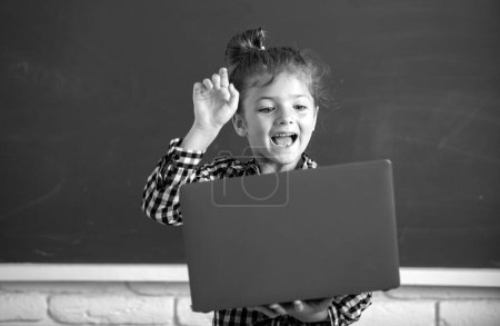 Photo for Excited student girl using laptop computer in school class on blackboard - Royalty Free Image