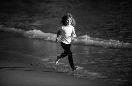 Téléchargez les photos : Joyeux garçon courir à la mer. L'enfant s'amuse sur la plage, géré par la piscine d'eau de mer. Vacances d'été avec enfant - en image libre de droit