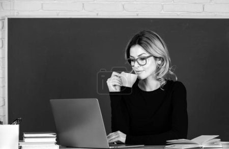 Téléchargez les photos : Portrait of teacher or female tutor working at table and drinking coffee in college or high school. Young women student studying in class - en image libre de droit