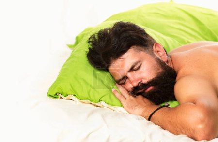 Foto de Un hombre guapo en la cama. Hombre barbudo durmiendo en la cama en el dormitorio. Buenos días. Joven durmiendo en la cama con almohadas en casa - Imagen libre de derechos