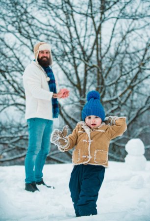 Foto de Feliz padre e hijo juegan en invierno en Navidad. Padre e hijo juegan con bola de nieve sobre fondo blanco de invierno - Imagen libre de derechos