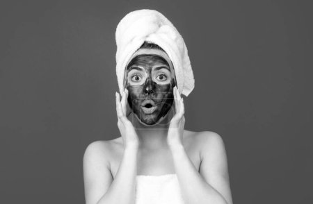 Photo for Surprised woman with mud facial mask, face clay mask spa. Beautiful woman with cosmetic mud facial procedure, spa health concept. Skin care beauty treatment. Towel on head. Medical mineral mud - Royalty Free Image