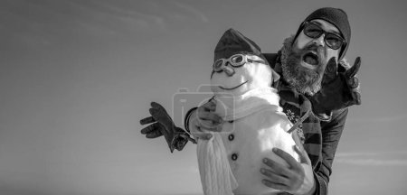 Foto de Hombre excitado con muñeco de nieve sobre fondo de invierno al aire libre. Hombre de nieve para bandera de invierno - Imagen libre de derechos