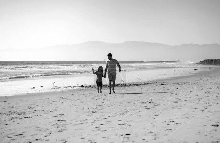Foto de Papá y su hijo tomados de la mano y caminando juntos. Padre e hijo caminando sobre el mar. Viajes en familia, vacaciones, padres concepto de día - Imagen libre de derechos