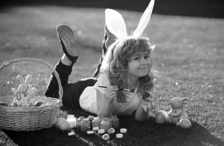Téléchargez les photos : Des enfants qui fêtent Pâques, peignent des œufs. Enfant en costume de lapin avec oreilles de lapin en plein air - en image libre de droit