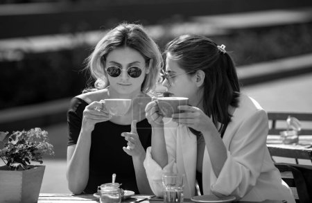 Foto de Amigos en la cafetería al aire libre. Retrato al aire libre de dos jóvenes hermosas amigas tomando café. Dos hermosas chicas con tazas de café en la cafetería de verano. Hermosas mujeres que se encuentran en la cafetería - Imagen libre de derechos