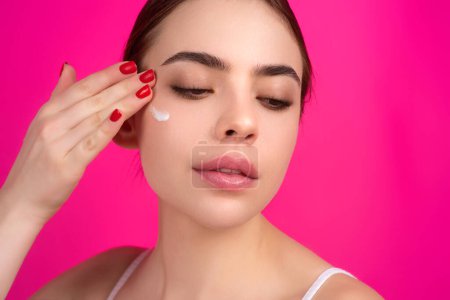 Photo for Close up facial cream on cheek. Beauty portrait of a beautiful half naked woman applying face cream isolated on studio background. Skin care product. Moisturizing creme on face - Royalty Free Image