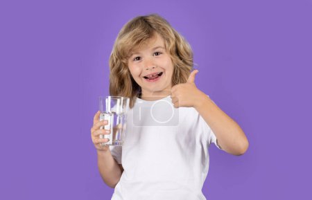 Photo for Kid drinking a fresh glass of water, isolated on studio background. Thirsty kid holding glass drinks water. Dehydration, hydration, water balance. Portrait of child drinking pure water from glass - Royalty Free Image