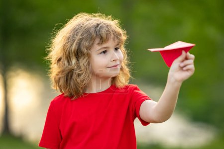Photo for Kid with plane. Child throwing paper plane. Cute blonde child play with paper plane outdoor. Child playing with paper plane in summer garden. Kid throwing paper planes in park. Childhood - Royalty Free Image