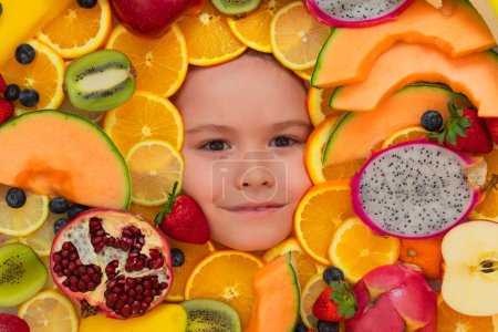 Photo for Healthy food background. Studio photo of different fruits with kids face. Mix of different fruits and berries. Cute little boy eats fruits. Kid eating vitamins. Close up kids face - Royalty Free Image