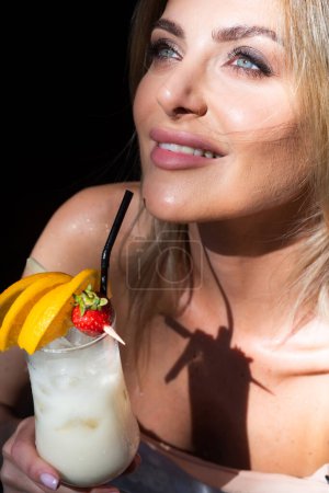Photo for Young girl with blue eyes drinking a cocktail. Summer refreshment. Woman face, fashion stylish female portrait. Beautiful woman drink cocktail in bar at night - Royalty Free Image