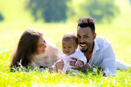 Photo for Multiethnic parents and mixed race baby in park. Multiethnic family outdoor portrait. Biracial baby child on yard. Diverse Multiethnic family. Multiethnic father and mother with child lying on grass - Royalty Free Image