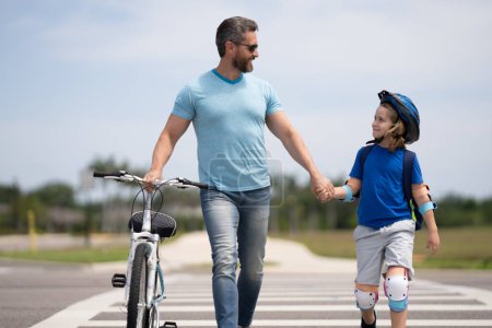 Photo for Kids insurance. Safety on road. Pedestrian crossing for cyclists. Happy playful dad with excited kid son riding a bicycle on weekend. Sporty family. Fathers day. Father teaching and support child - Royalty Free Image