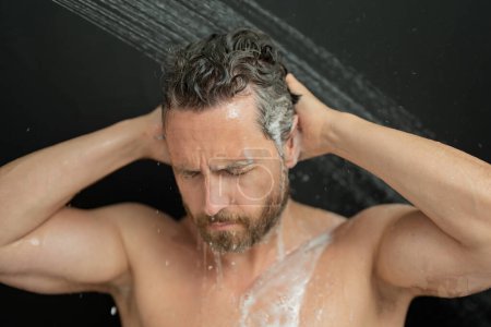 Foto de Retrato de hombre lavando el cabello con champú tomando ducha. Lavar el cabello con champú. Hombre lavando el cabello con champú anti-caspa, tomando una ducha. Producto para el cuidado del cabello, gel de espuma, champú y loción - Imagen libre de derechos