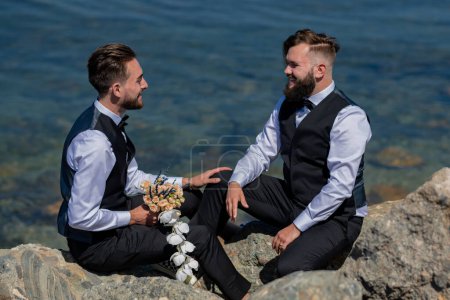 Foto de Los novios gay caminando juntos en la playa del mar durante el día de la boda. Retrato de pareja gay enamorada el día de la boda. gay boda al aire libre - Imagen libre de derechos