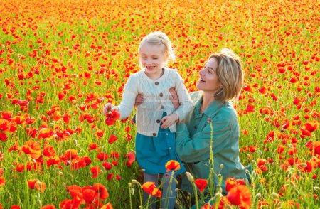 Foto de Madre e hija están jugando en el campo de las amapolas rojas florecientes. Feliz maternidad. - Imagen libre de derechos