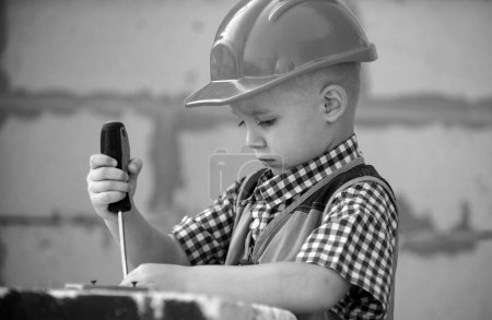 Photo for Kid boy twists bolt with screwdriver. Child repairman with repair tool. Child in helmet and boilersuit on construction site. Little worker engineer. Repair home - Royalty Free Image