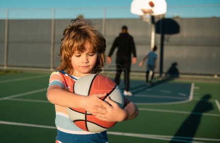 Foto de Lindo chico sonriente juega baloncesto. Niños activos disfrutando de juego al aire libre con pelota cesta - Imagen libre de derechos