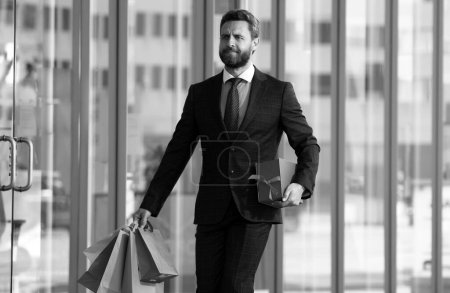 Foto de Hombre de negocios de compras en un centro comercial. Feliz hombre de negocios con traje y bolsas de papel. Hombre Shopaholic caminando en la calle comercial con un montón de bolsas de compras - Imagen libre de derechos