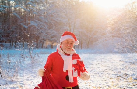 Téléchargez les photos : Père Noël souriant avec cadeau la veille de Noël à l'extérieur - en image libre de droit