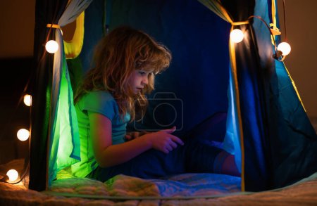 Téléchargez les photos : Enfant couché au lit et apprenant dans une classe virtuelle en ligne. Un gamin qui travaille sur Internet à la maison. Enfant utilisant un ordinateur portable. L'enseignement à domicile pour les enfants - en image libre de droit