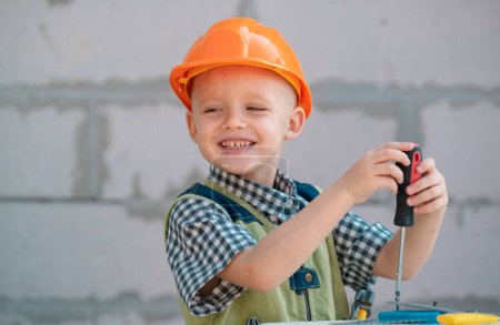 Photo for Little boy holding screwdriver. Happy smiling kid twists bolt with screwdriver. Little Repairman with repair tool. Cute kid as a construction worker. Childrens play with screwdriver - Royalty Free Image