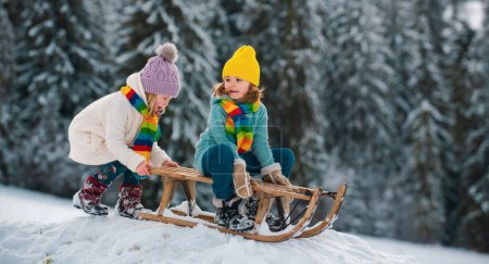 Téléchargez les photos : Des enfants heureux s'amusent et chevauchent le traîneau dans la forêt enneigée d'hiver. Vacances de Noël d'hiver et week-end d'hiver actif, activités pour enfants - en image libre de droit