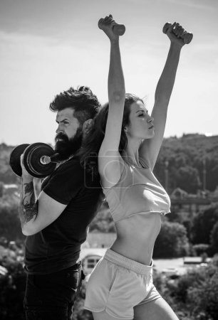 Photo for Man and woman training with dumbbells, athletic sport couple exercise outdoor. Fitness sexy models pumping up arm with dumbbell - Royalty Free Image