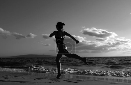 Foto de Una mujer corriendo en la playa. Joven chica sana correr al amanecer playa - Imagen libre de derechos