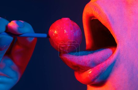 Foto de Sexy mamada símbolo. Piruleta lamiendo la boca, labios brillantes femeninos rojos y piruleta de caramelo rosa - Imagen libre de derechos