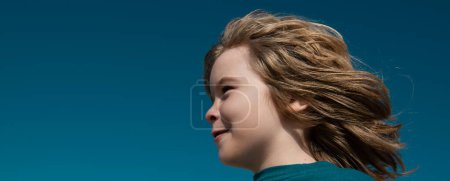 Téléchargez les photos : Portrait d'un petit garçon blond regardant loin sur le ciel bleu avec l'espace de copie, bannière de gros plan. Joli visage d'enfant. Enfant émotionnel positif - en image libre de droit